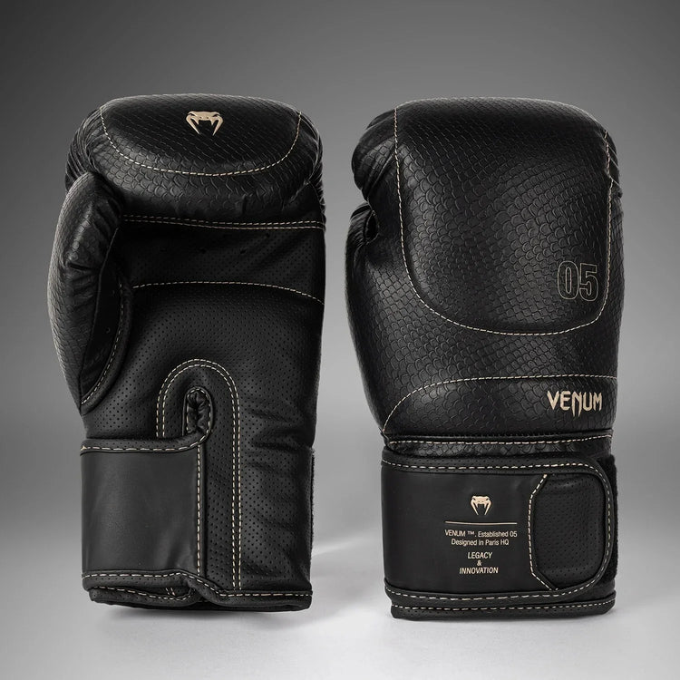 Black Venum boxing gloves with textured finish, white stitching, and velcro strap, studio background