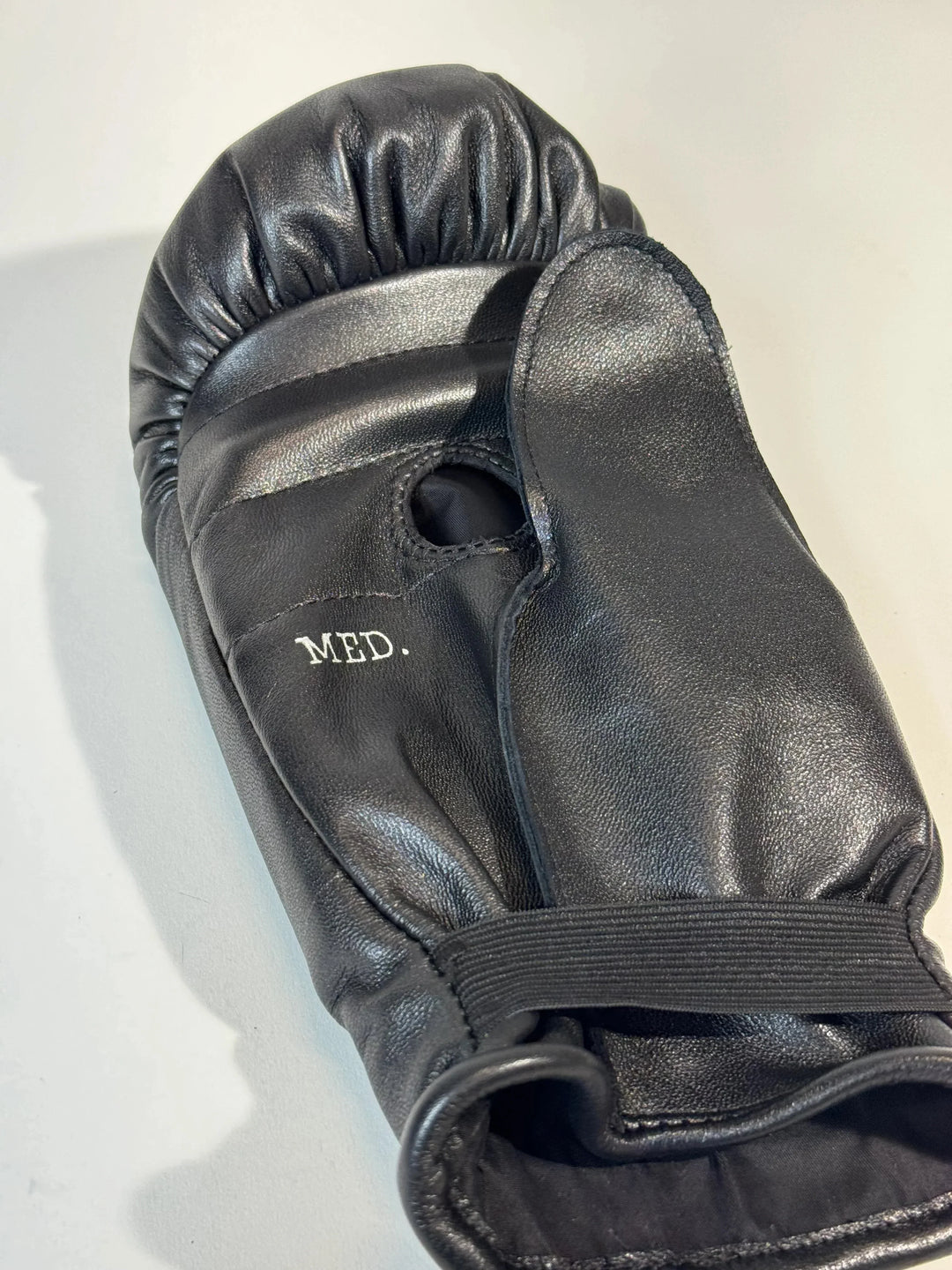 Black leather boxing glove with thumb grip and 'MED.' size marking on a light background