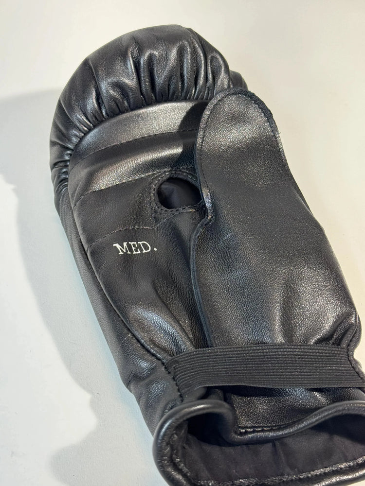 Black leather boxing glove with thumb grip and 'MED.' size marking on a light background
