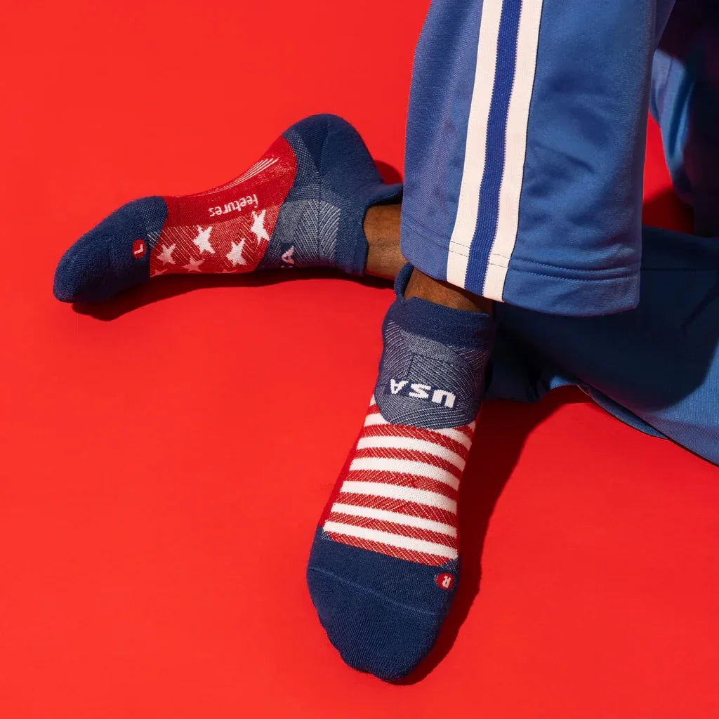 Person wearing USA flag athletic socks and blue track pants on red background