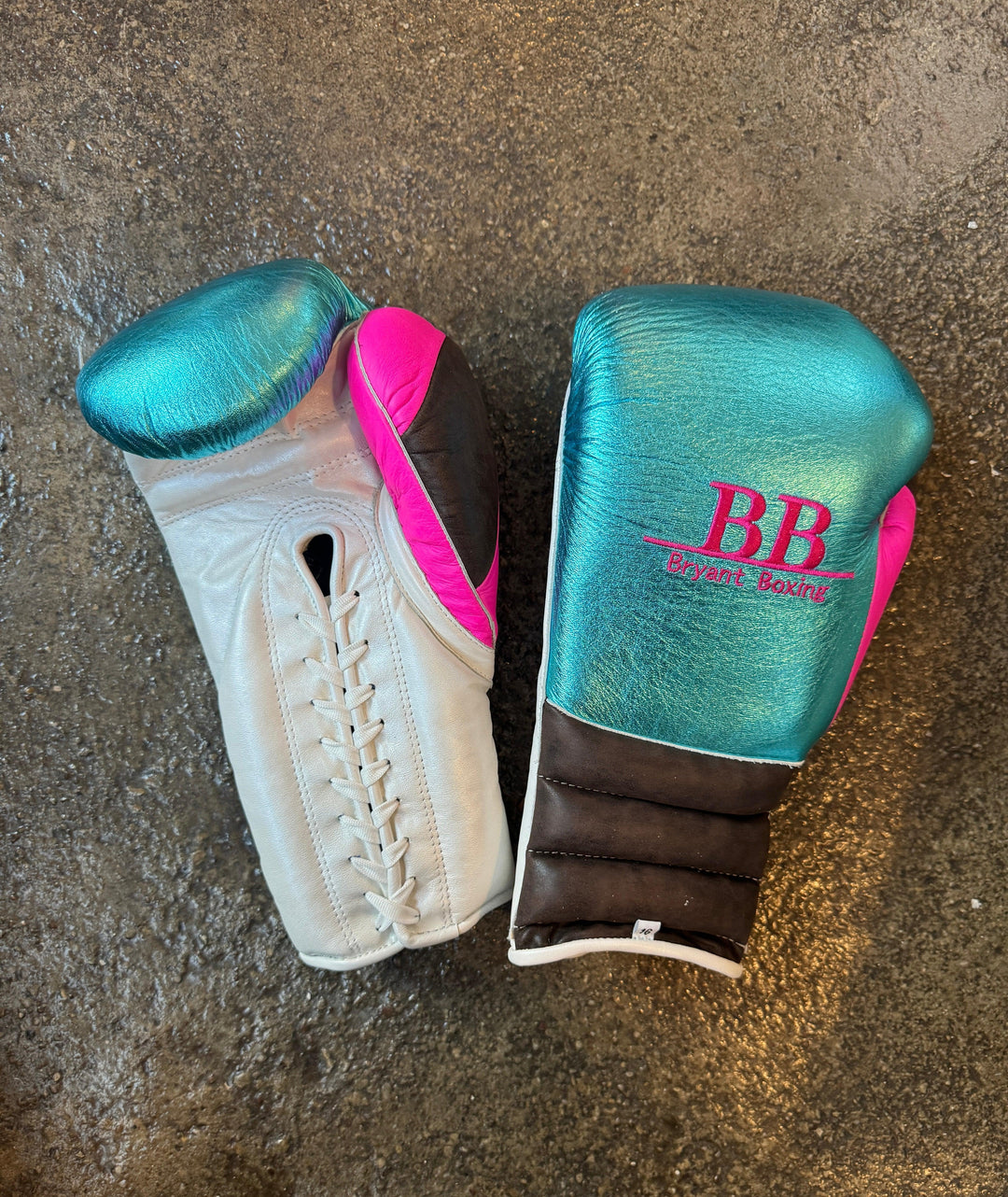 Pair of teal, pink, and white lace-up boxing gloves with BB Bryant Boxing logo on concrete