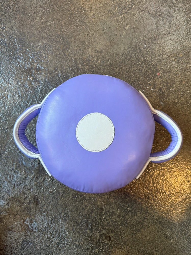 Purple round boxing pad with white handles and target spot on textured gym floor