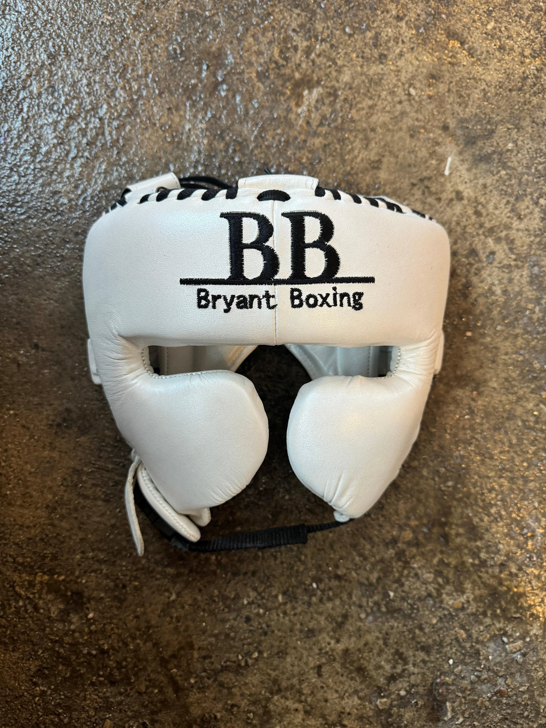 White Bryant Boxing headgear with black stitching on a textured floor