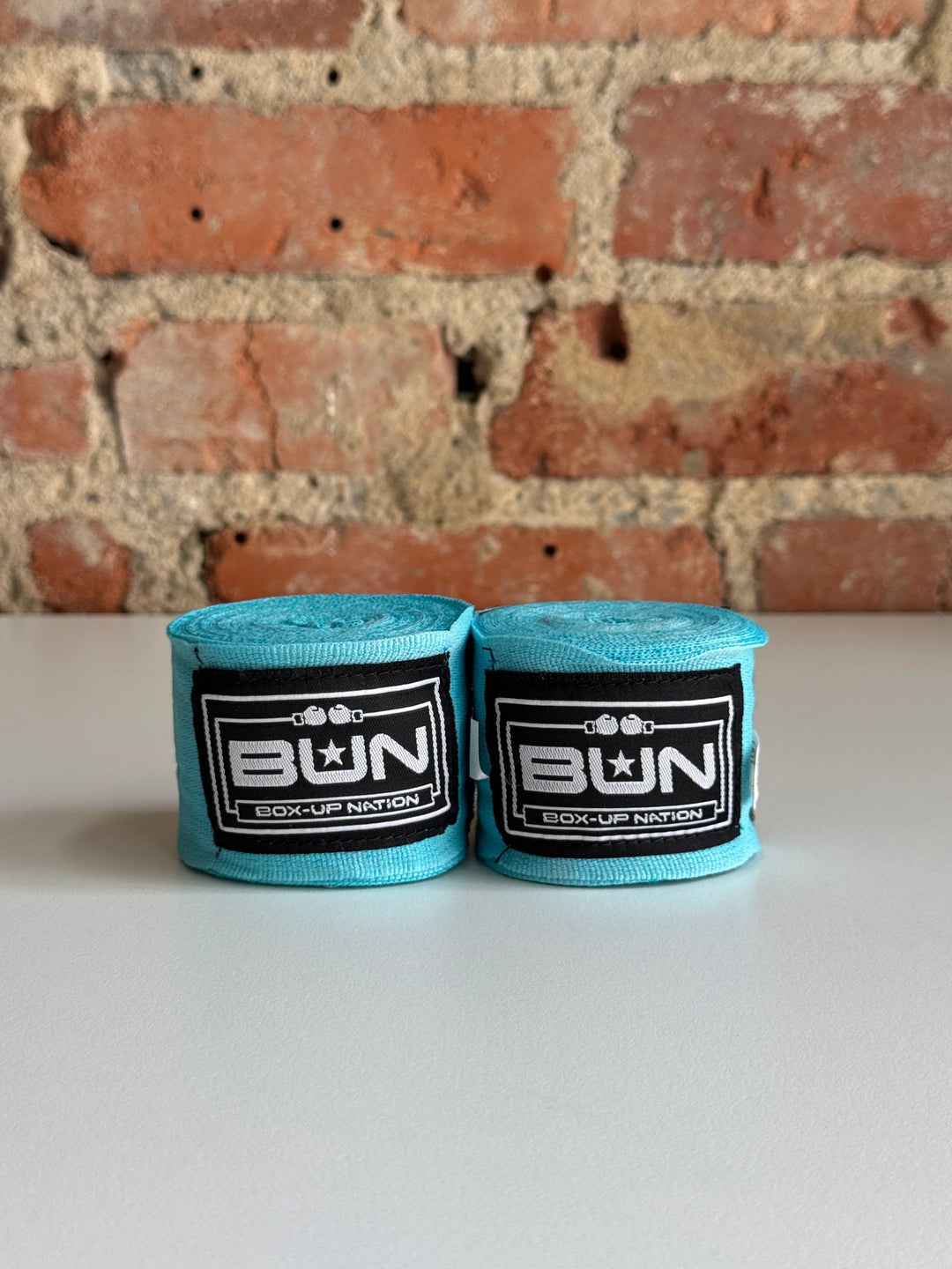 Pair of aqua blue boxing hand wraps with logo on table, exposed brick wall background