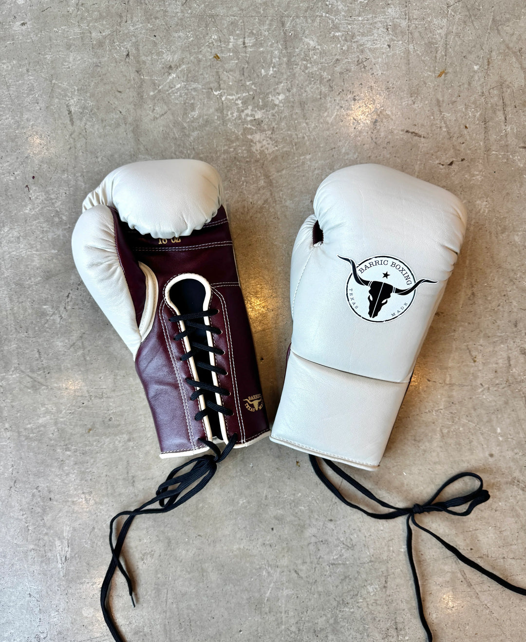 Pair of lace-up boxing gloves in white and maroon on a concrete floor