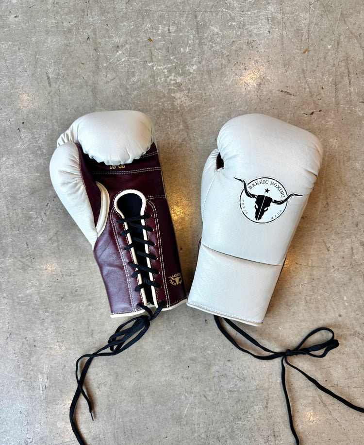 Pair of lace-up boxing gloves in white and maroon on a concrete floor