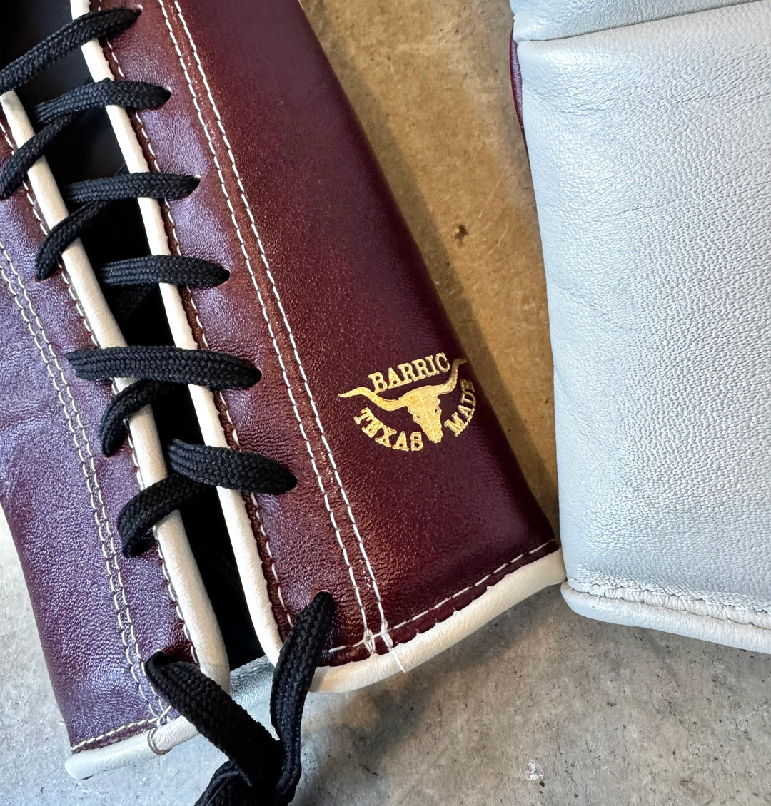 Close-up of maroon lace-up leather boxing glove with Texas Made Barric logo, on concrete.