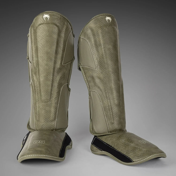 Pair of olive green kickboxing shin guards with textured finish on gray background
