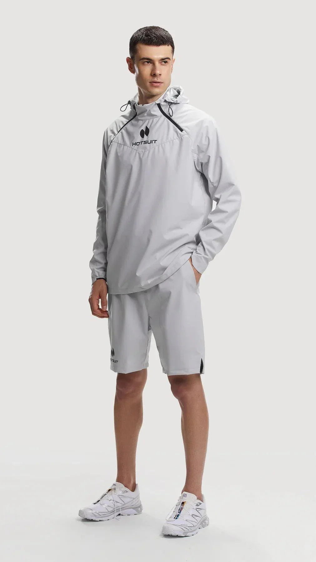 Man wearing gray HOTSUIT temp control sauna suit with hoodie and shorts, standing on white background