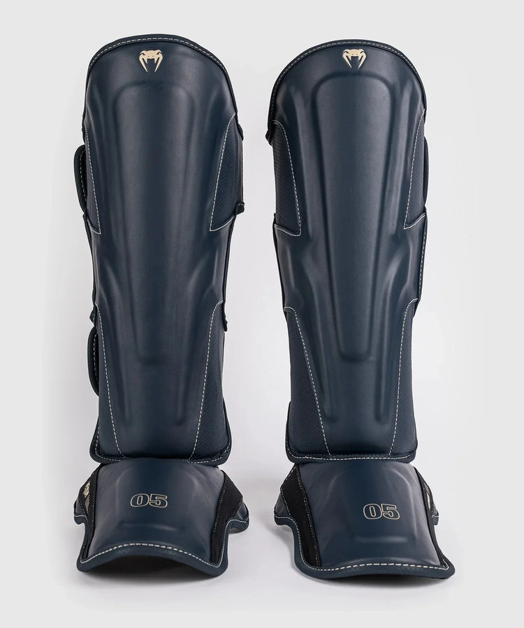 Pair of blue boxing shin guards with reinforced padding and white stitching on a plain background